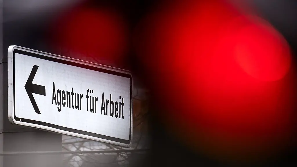 Eine-rote-Ampel-leuchtet-vor-einem-Schild-das-auf-die-Agentur-fuer-Arbeit-hinweist