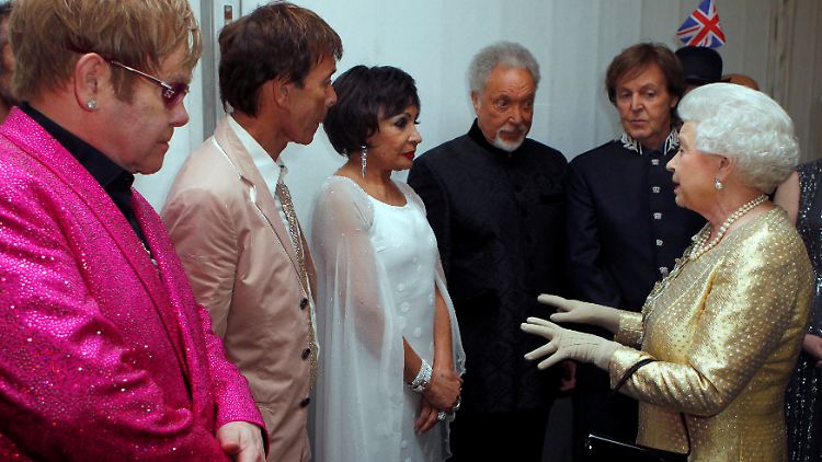 Im Jahr 2012 ist Queen Elizabeth II. umringt von legendären britischen Popstars. Paul McCartney (neben der Queen) macht einige Jahre später in Anwesenheit der Königin einen Witz, über den sie sich offenbar amüsierte.