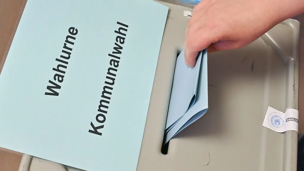 Eine-Person-steckt-ihren-Stimmzettel-in-eine-Wahlurne-mit-der-Aufschrift-Wahlurne-Kommunalwahl