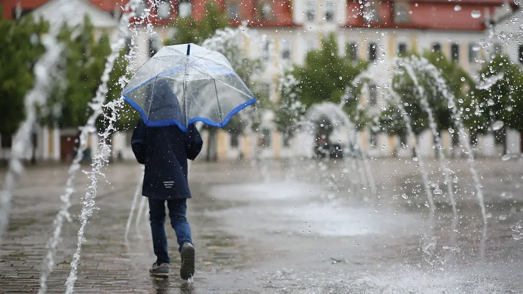 Ein-Kind-geht-mit-einem-Schild-bei-Regenwetter-durch-ein-Wasserspiel-auf-dem-Domplatz