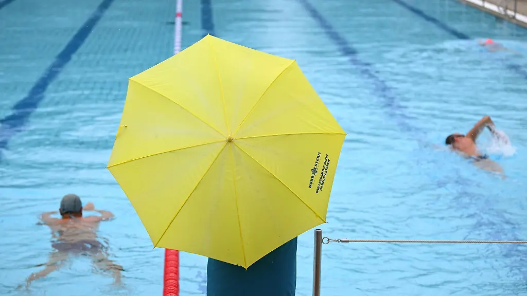 Eine-Frau-steht-bei-Regenwetter-mit-Schirm-am-Rand-des-Schwimmerbeckens