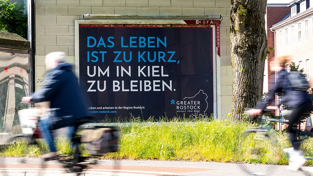 Ein-Plakat-mit-der-Aufschrift-Das-Leben-ist-zu-kurz-um-in-Kiel-zu-bleiben-haengt-an-einem-Haus