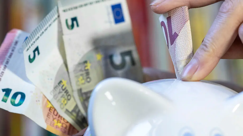 Eine-Frau-steckt-einen-10-Euroschein-in-ein-Sparschwein