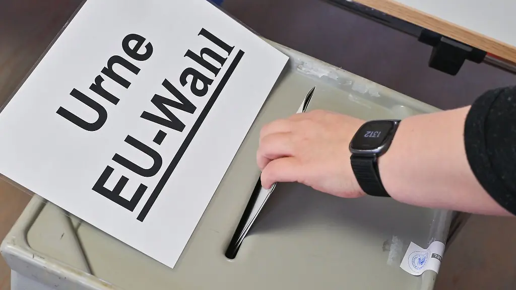 Eine-Person-steckt-ihren-Stimmzettel-in-eine-Wahlurne-mit-der-Aufschrift-Urne-EU-Wahl