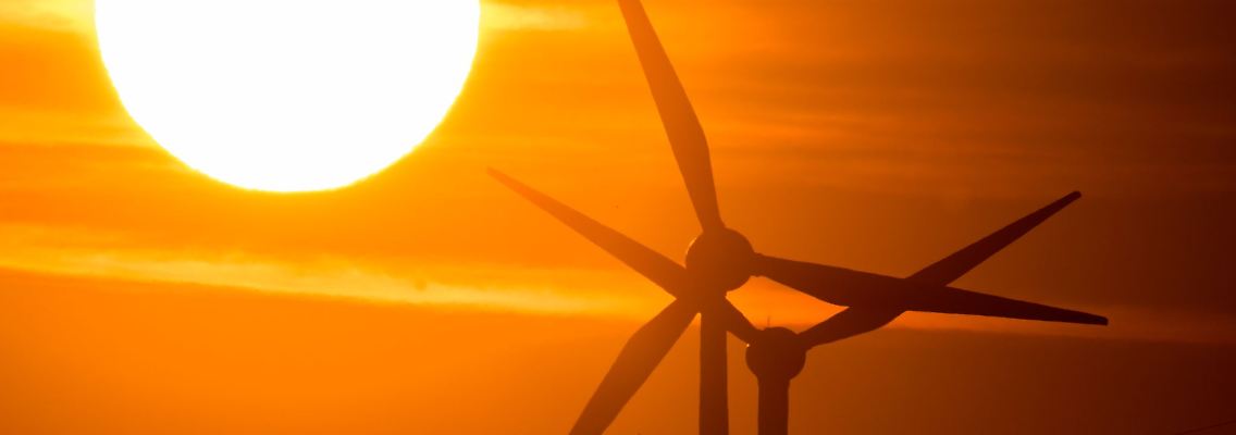 Die Sonne geht hinter Windrädern auf.