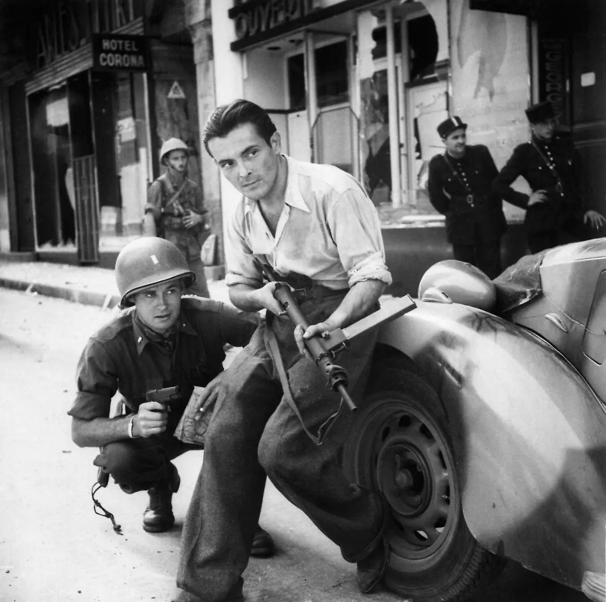 American-officer-and-French-partisan-crouch-behind-an-auto-during-a-street-fight-in-a-French-city-NARA-531322-restored-by-Buidhe