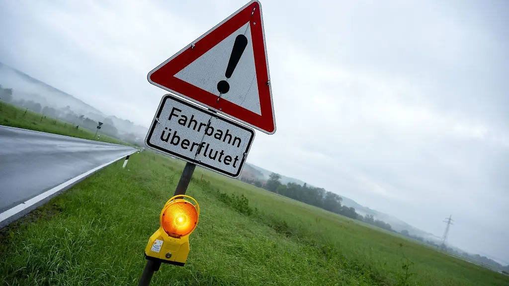 Ein-Schild-warnt-vor-Hochwasser-die-Strasse-dahinter-ist-ueberflutet