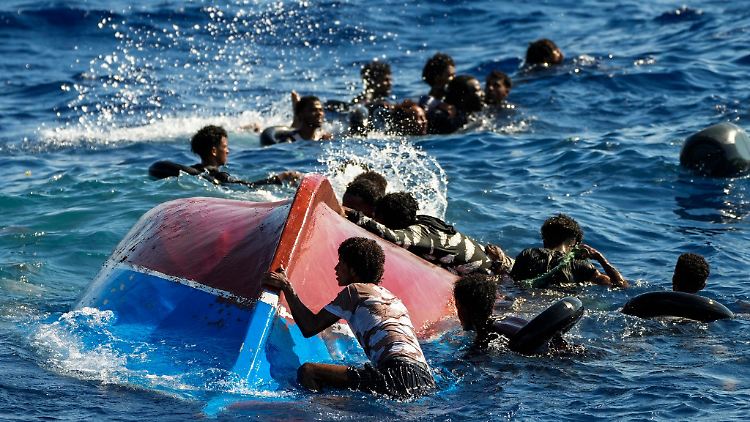 Migranten schwimmen neben ihrem umgestürzten Holzboot im Mittelmeer (Archivbild).