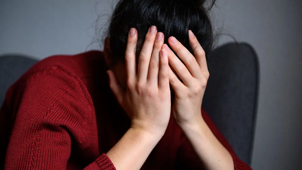 Eine-Frau-sitzt-mit-dem-Kopf-in-den-Haenden-auf-einem-Stuhl-gestellte-Szene