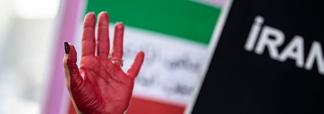 Eine rot bemalte Hand einer Frau erhebt sich zwischen Plakaten während einer Demonstration.
