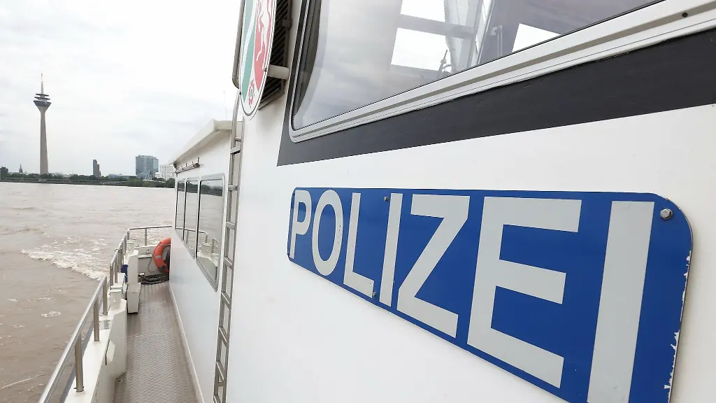 Ein-Schild-mit-dem-Aufschrift-Polizei-ist-an-einem-Boot-der-Wasserschutzpolizei-angebracht-auf-dem-ein-Pressetermin-zum-Praeventionskonzept-Sensibilisierung-ueber-Gefahren-beim-Baden-in-Fliessgewaessern-vorgestellt-wird