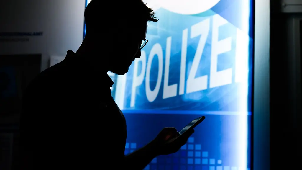 Ein-Polizist-steht-mit-einem-Smartphone-in-der-Praeventionsstelle-Cyberkriminalitaet