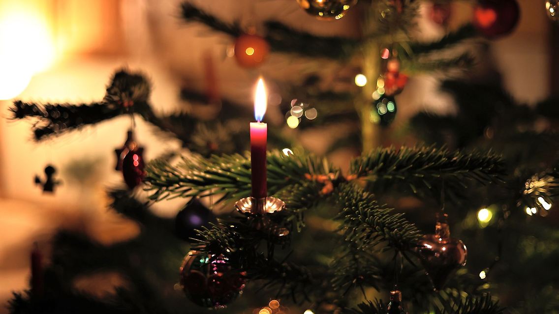 Eine Kerze brennt an einem festlich geschmückten Weihnachtsbaum.