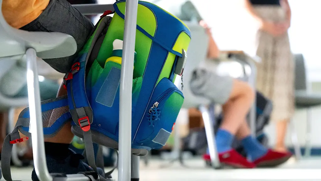 Ein-Rucksack-haengt-im-Klassenzimmer-am-Tisch-eines-Grundschuelers