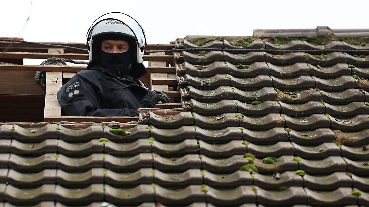 Ein Polizist besteigt das Dach eines besetzten Hauses in Lützerath.