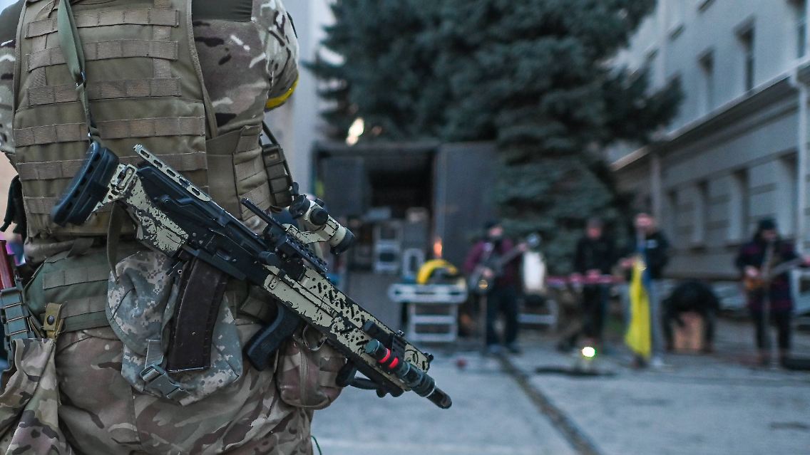 In Cherson bewacht ein Soldat den Auftritt einer Band. Stunden zuvor sind dort russische Raketen eingeschlagen.