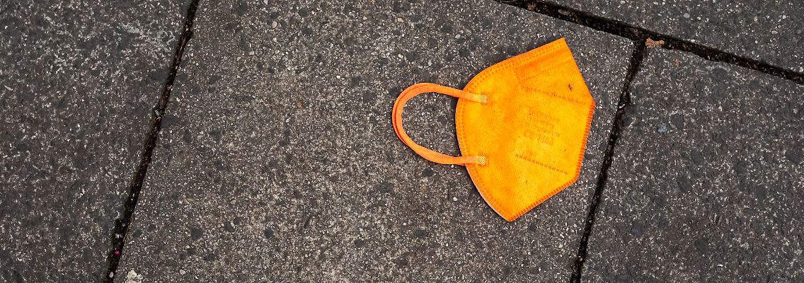 Ein gebrauchter orangefarbener Mund-Nasen-Schutz liegt auf dem Gehweg.