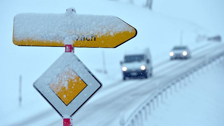 Neuschnee bedeckt ein Vorfahrtsschild und einen Wegweiser.