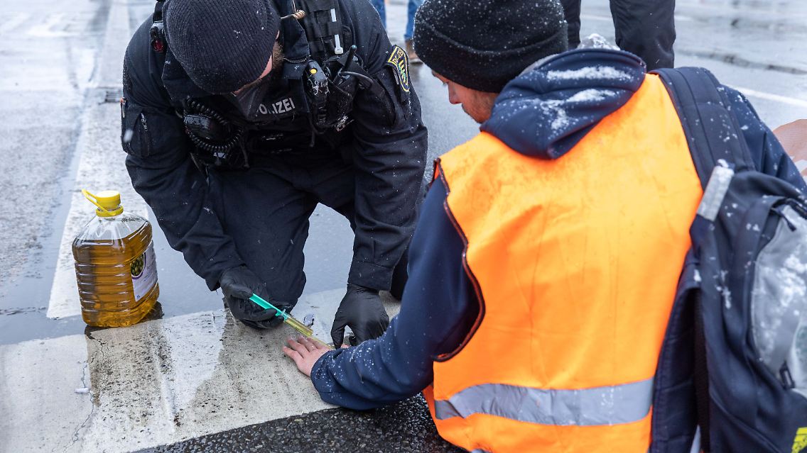 Ein Polizist nutzt Olivenöl, um einen angeklebten Aktivisten von der Straße wieder zu lösen.
