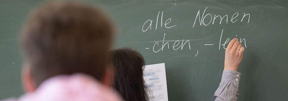 Ein Lehrerin schreibt im Unterricht etwas an die Tafel.