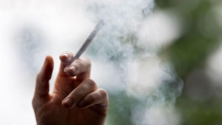 Ein Mann hält einen Joint in der Hand.