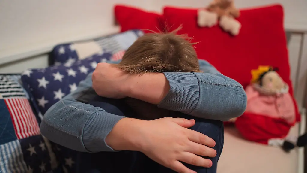 Ein-Junge-kauert-sich-auf-seinem-Bett-zusammen