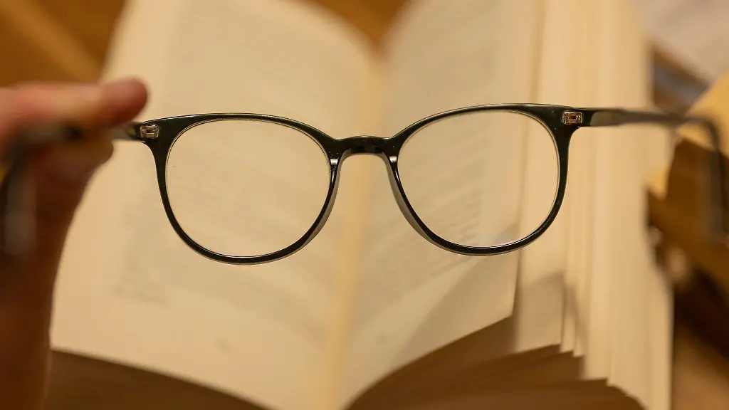 Ein-Mann-haelt-eine-Lesebrille-vor-einem-geoeffneten-Papierbuch