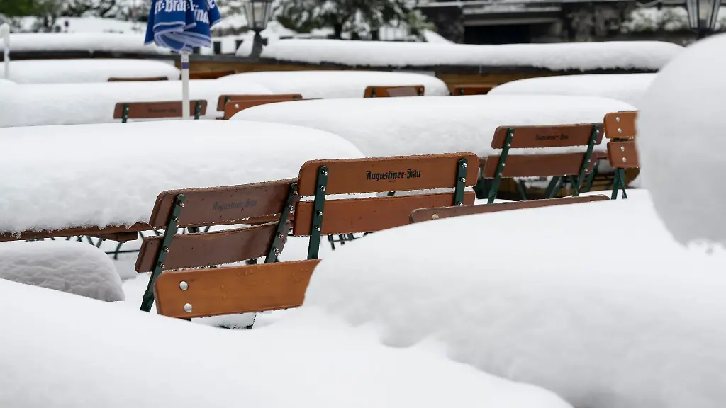 Schnee-liegt-auf-Tischen-und-Stuehlen-in-einem-Biergarten-am-Walchensee