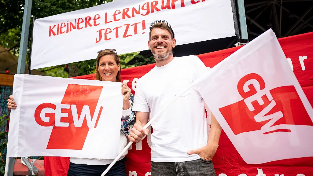 Sven-und-Bianca-beide-Lehrer-an-einer-Neukoellner-Schule-stehen-mit-zwei-GEW-Flaggen-beim-Warnstreik