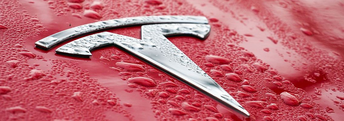Das Tesla-Logo ist auf der Motorhaube eines roten Pkws zu sehen.