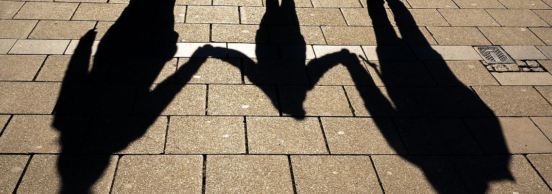 Die Schatten von zwei Erwachsenen und einem Kind fallen in den Morgenstunden auf den Asphalt.