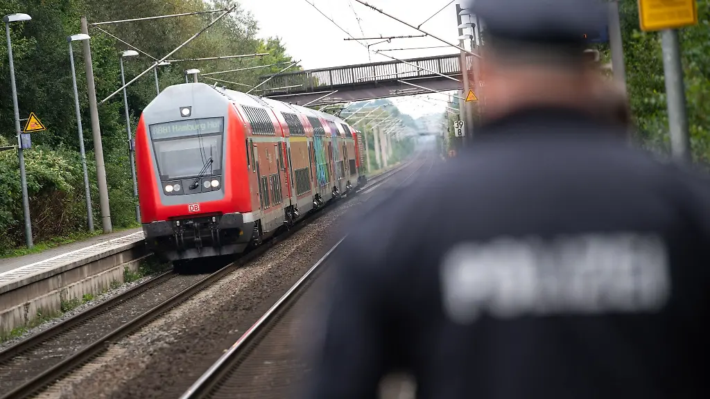 Ein-Polizist-laeuft-ueber-einen-Bahnsteig-waehrend-im-Hintergrund-ein-doppelstoeckiger-Regionalzug-einfaehrt