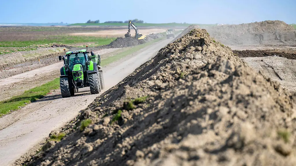 Ein-Traktor-faehrt-an-einer-Baustelle-an-einem-Deich-vorbei