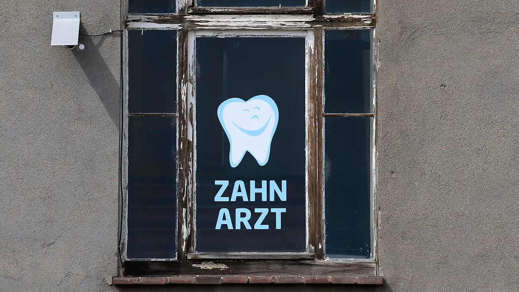 Zahnarzt-steht-an-einem-Fenster-eines-Hauses-in-dem-sich-eine-Zahnarztpraxis-befindet-geschrieben