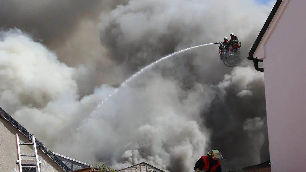 Einsatzkraefte-der-Feuerwehr-versuchen-den-Brand-im-Dachstuhl-einer-Lagerhalle-zu-loeschen