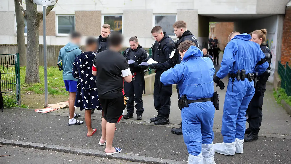 Polizisten-zum-Teil-in-Schutzkleidung-kontrollieren-Anwohner-vor-einem-Wohnkomplex