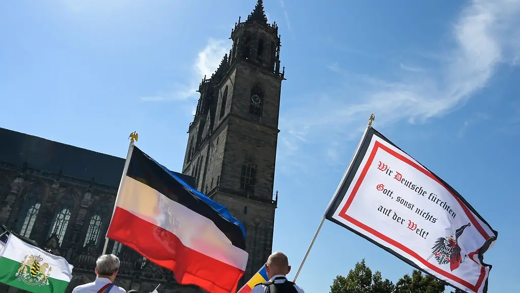 Die-Reichsflagge-und-eine-Fahne-mit-der-Aufschrift-Wir-Deutschen-fuerchten-Gott-sonst-nichts-auf-der-Welt-wird-vor-dem-Magdeburger-Dom-bei-einer-Demonstration-der-Reichsbuerger-Szene-hochgehalten