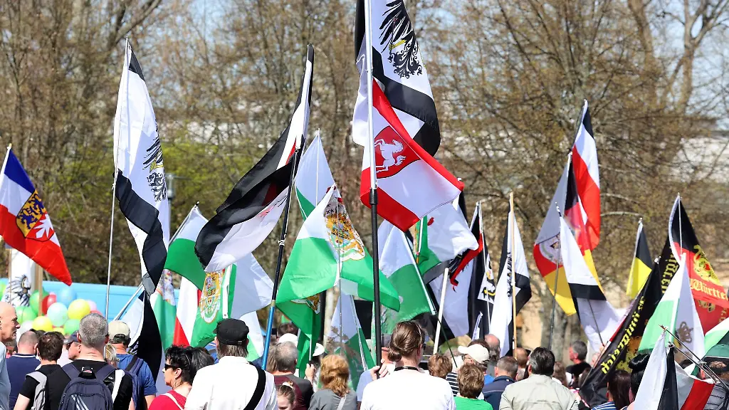 Teilnehmer-einer-Kundgebung-von-Reichsbuergern-stehen-mit-Fahnen-auf-dem-Versammlungsplatz