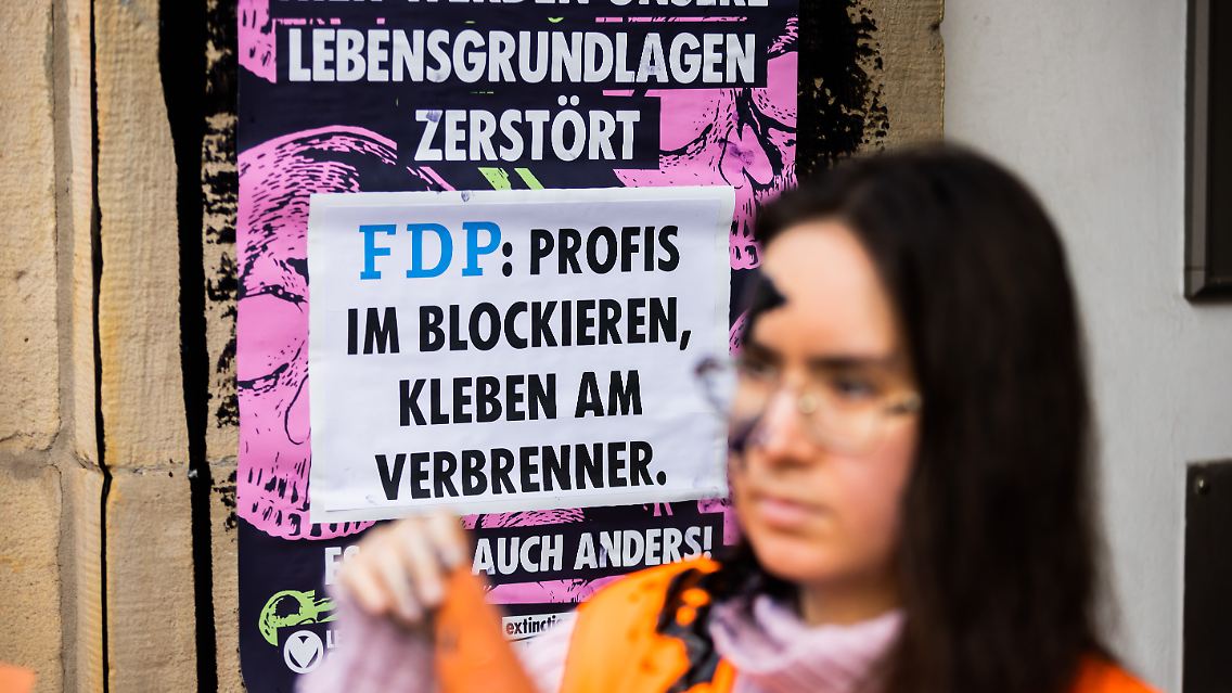 Eine Aktivistin der Klimagruppe "Letze Generation" steht vor der FDP-Bundesgeschäftsstelle. Auch ihr Gesicht ist mit der Öl-ähnlichen Flüssigkeit beschmiert.