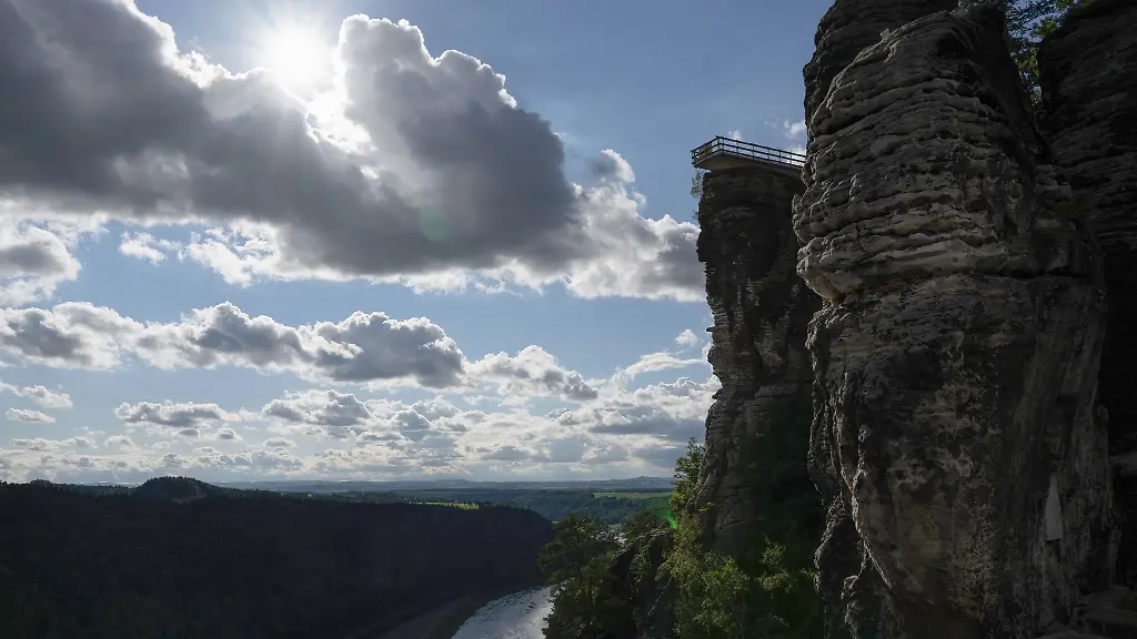Der-neue-Aussichtssteg-der-Bastei-zeichnet-sich-im-Elbsandsteingebirge-im-Nationalpark-Saechsische-Schweiz-im-Gegenlicht-der-Sonne-als-Silhouette-ab