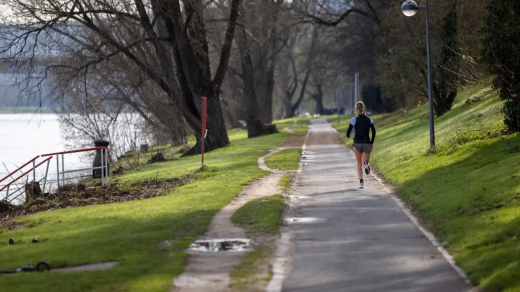 Ein-Laeuferin-joggt-am-fruehen-Sonntagmorgen-bei-sonnigem-Wetter-am-Rhein-vorbei