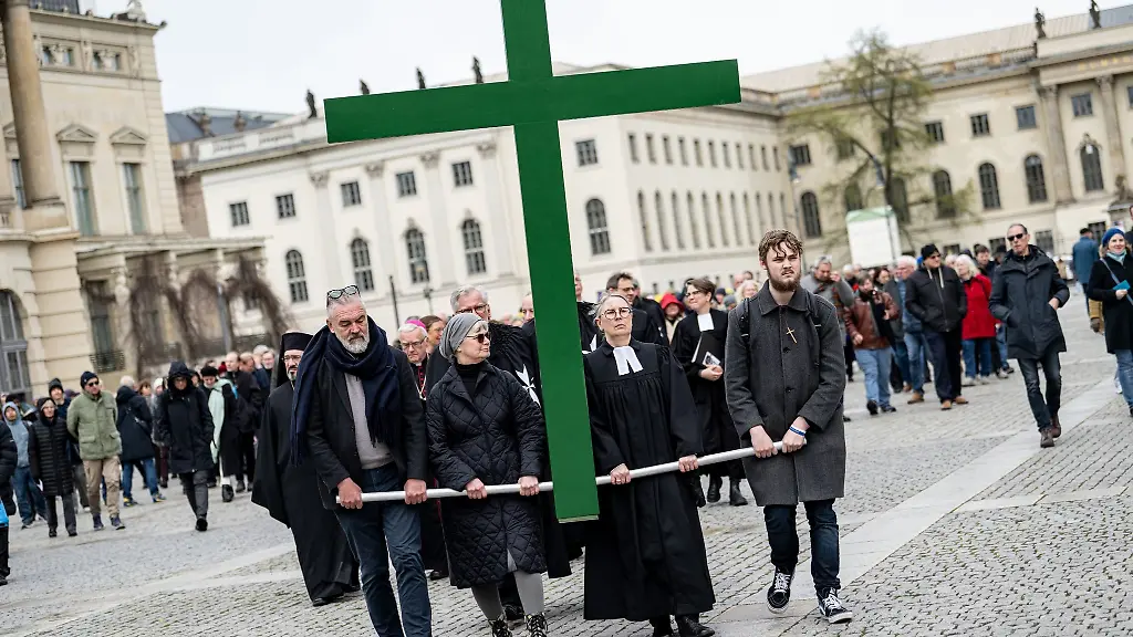 Glaeubige-tragen-bei-der-Karfreitagsprozession-der-St-Marienkirche-ein-gruenes-Kreuz-ueber-den-Bebelplatz