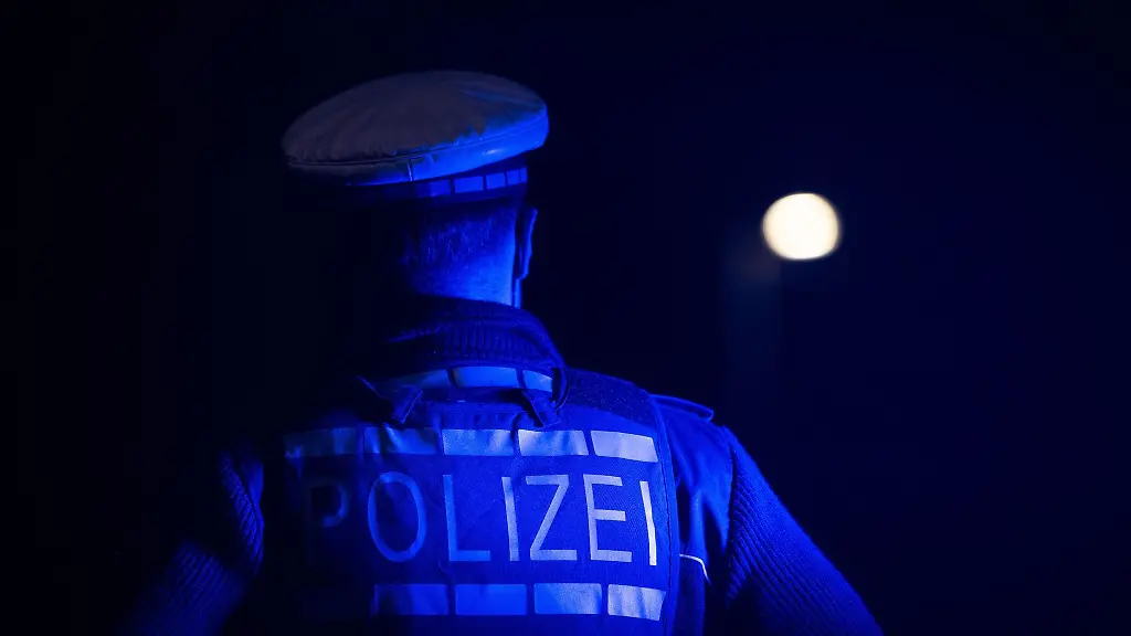 Ein-Polizist-steht-im-Rahmen-eines-Fototermins-neben-einem-Polizeifahrzeug-gestellte-Szene