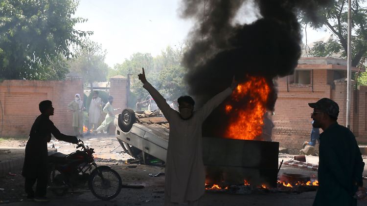 Anhänger des pakistanischen Ex-Premierministers Khan stehen neben einem brennenden Auto in Peshawar.