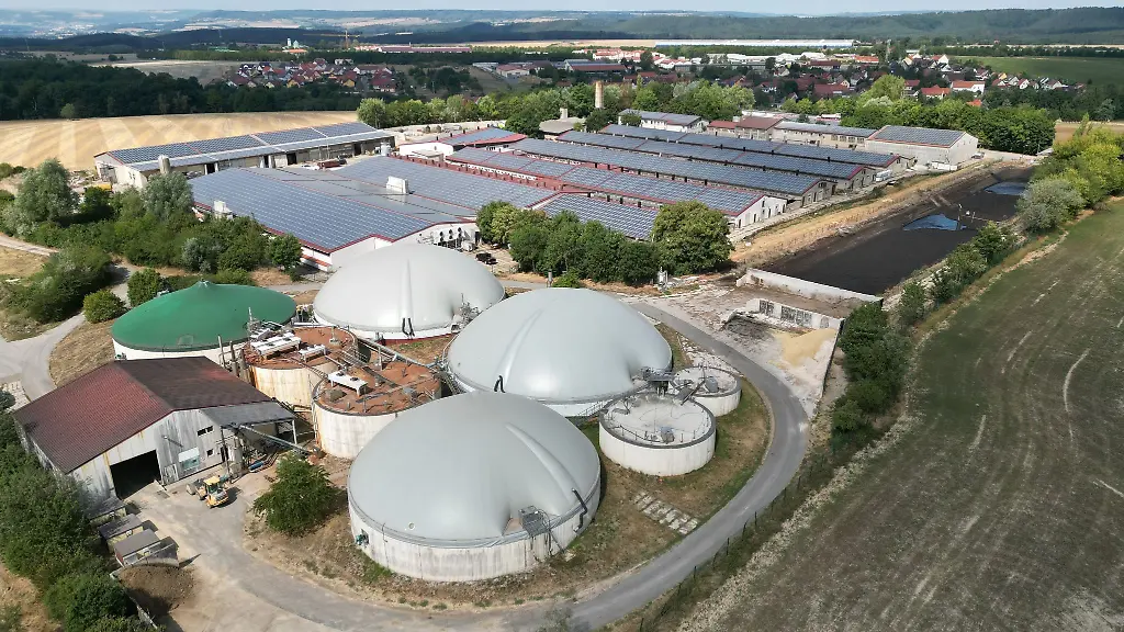 Blick-auf-eine-Biogasanlage-einer-Agragenossenschaft-Dahinter-sind-Gebaeude-mit-Solarpanelen-zu-sehen