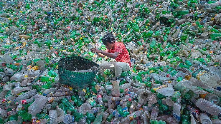 In Bangladesch sitzt ein Mitarbeiter einer Recyclingfabrik auf einem Haufen Plastikflaschen und sortiert diese.