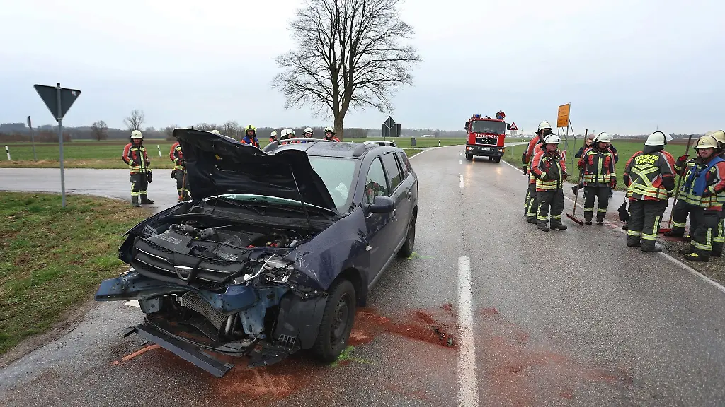 Einsatzkraefte-der-Feuerwehr-stehen-neben-einem-beschaedigten-Auto-an-der-Unfallstelle