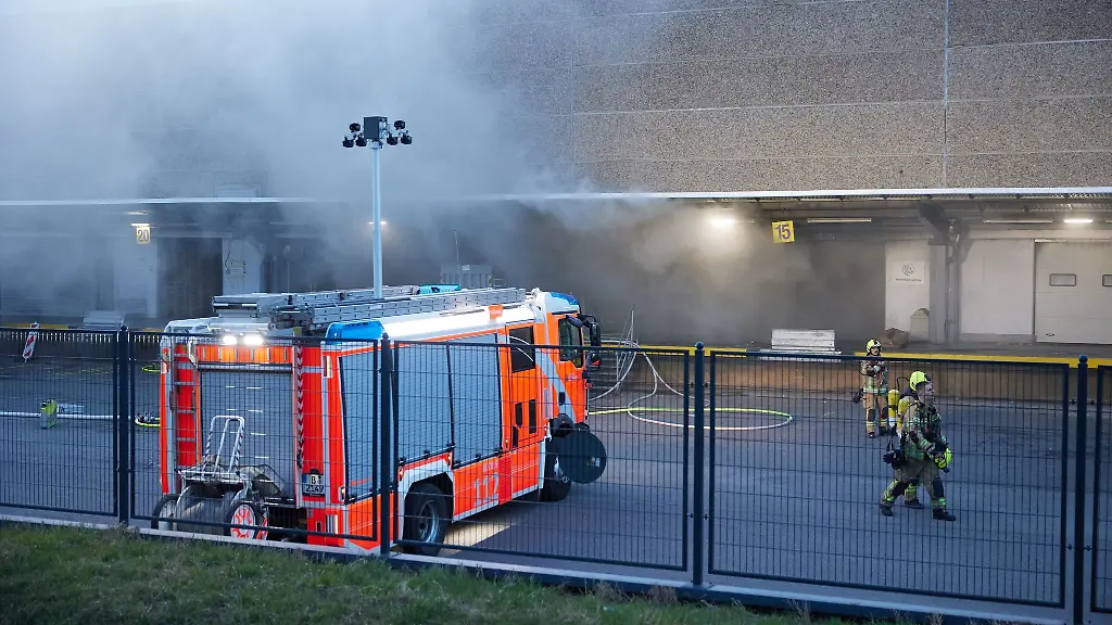 Feuerwehrkraefte-sind-dabei-ein-Feuer-in-einer-Lagerhalle-zu-loeschen