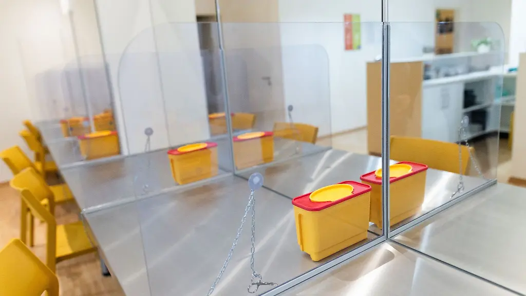 Ein-Container-fuer-gebrauchte-Nadeln-steht-in-einem-Drogenkonsumraum-auf-dem-Tisch