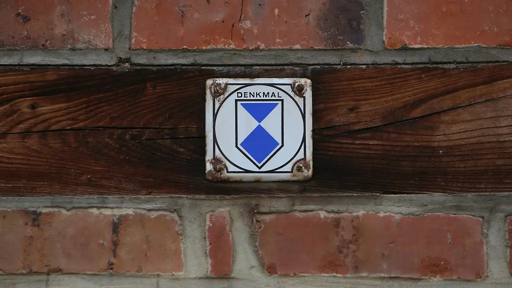 Eine-Plakette-mit-dem-Denkmalschutzlogo-ist-an-einem-Fachwerkhaus-befestigt